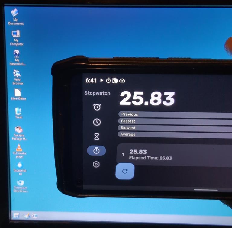 Photograph of a cell phone in front of a computer monitor, it has a timer which has 25.83 seconds on it. It's timing the boot of the device.